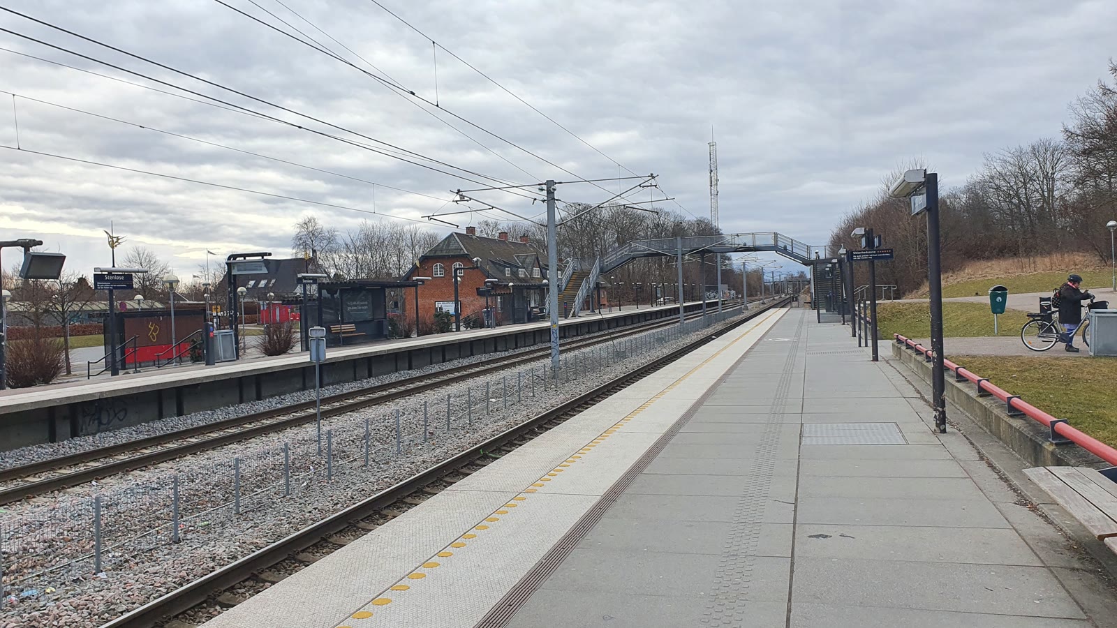 Perronen på Stenløse Station med den røde stationsbygning og en cyklist.