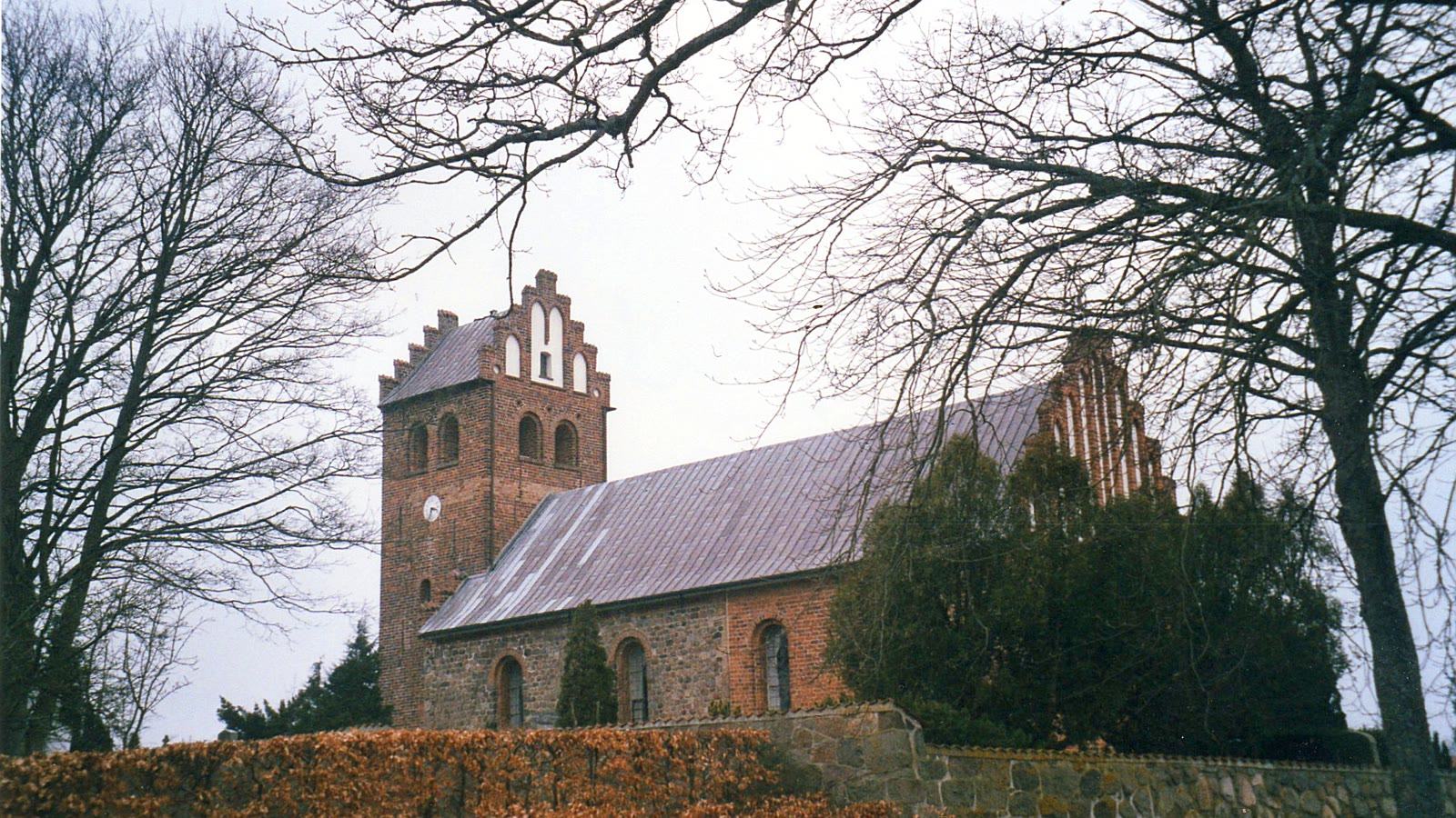 Stenløse Kirke set fra kirkegårdsdiget med kampestensmure og rødt teglstenstårn.